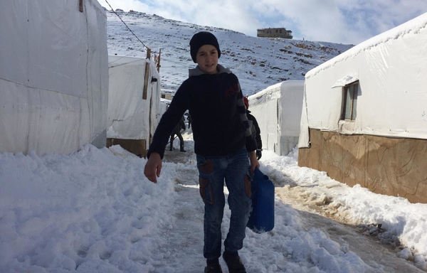 فتى يحمل وعاء ويتنقل في الثلج في أحد مخيمات اللاجئين السوريين في عرسال. [حقوق الصورة للجنة صوت اللاجئ السوري في لبنان على فيسبوك]