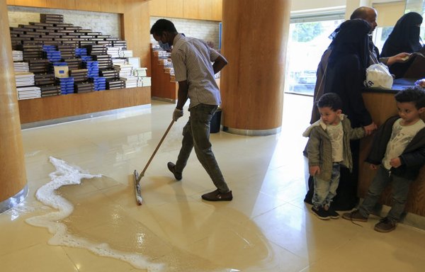 An employee, wearing a protective mask as a measure against COVID-19, mops the floor at a pastry shop in Sanaa on March 19th. [Mohammed Huwais/AFP]