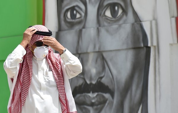 A Saudi man, wearing a mask as a precaution against COVID-19, walks past a mural of King Salman bin Abdulaziz in Riyadh on March 15th. [Fayez Nureldine/AFP]