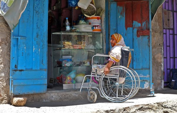 Jamila Qassem Mahyoub, a Yemeni woman whose legs were amputated after stepping on a landmine while herding her sheep in 2017, sits in a wheelchair outside her shop in Yemen's city of Taez on March 20th, 2019. [Ahmad al-Basha/AFP]