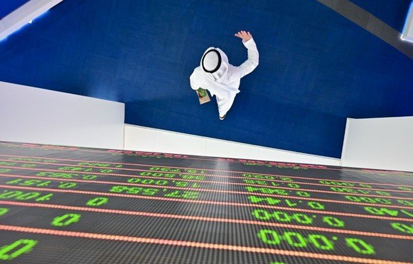 In this file photo taken on March 8th, a trader walks by beneath a stock display board at the Dubai Stock Exchange in the UAE. The Middle East and North Africa economy will contract by 3.3% this year, the IMF said April 14th. [Giuseppe Cacace/AFP]