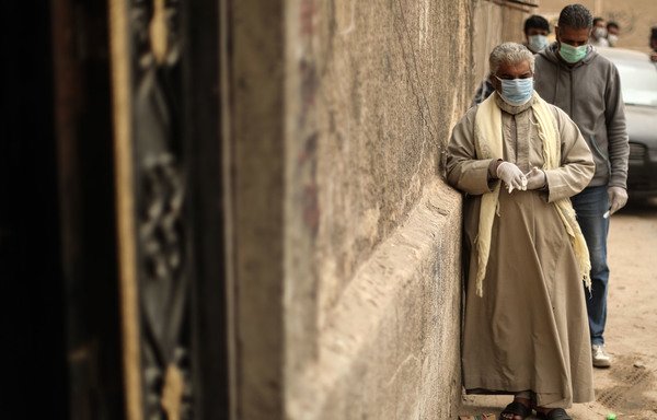 Egyptian men wearing masks wait outside the Egyptian Food Bank in Cairo to receive aid on April 5th, as the charity distributes aid to people who lost their jobs due to the coronavirus pandemic crisis.[Mohamed el-Shahed/AFP]