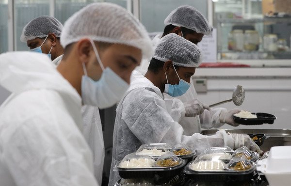 Qatar charity workers prepare food parcels on April 16th. A restaurant better known for fine dining has lent its facilities to Qatar Charity to feed migrant workers confined to an area of Doha's southern Industrial Area after the pandemic outbreak. [Karim Jaafar/AFP]