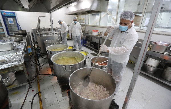 Qatar charity workers prepare food for migrant workers in a restaurant kitchen in Doha on April 16th. [Karim Jaafar/AFP]