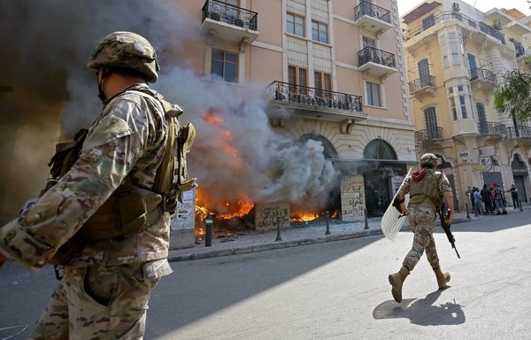 Lebanese soldiers clear the road next to a burning bank branch, set ablaze by demonstrators following the funeral in Tripoli of protestor Fawaz al-Samman on April 28th. [Ibrahim Chalhoub/AFP]