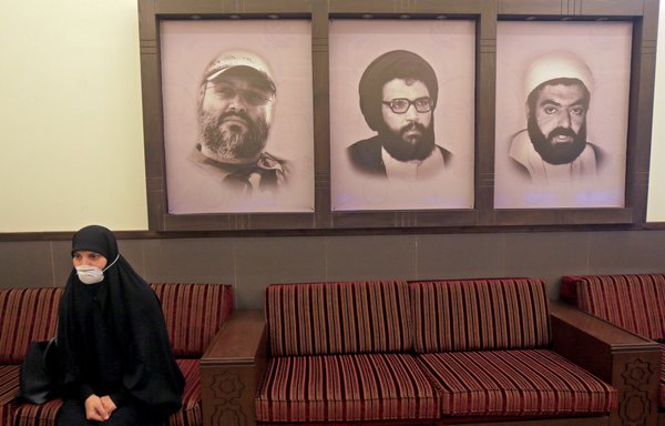 A picture taken during a guided tour organised by Lebanese Hizbullah shows a mask-clad woman sitting next to portraits of late Hizbullah leader Abbas Mussawi (centre), late commanders Imad Mughniyeh (left) and Ragheb Harb, at a centre in Beirut's southern suburbs on March 31st. [AFP]