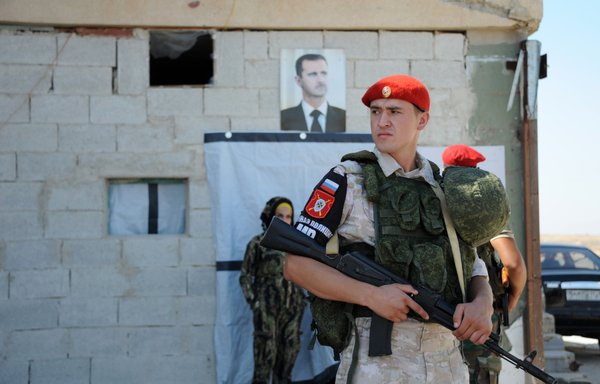 A Russian soldier stands guard outside a checkpoint in Syria in 2019 with a portrait of Syrian president Bashar al-Assad in the background. [Maxime Popov/AFP]
