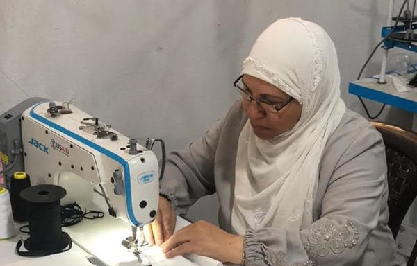 جميلة درويش في مشغلها في منطقة المنية الواقعة على الحدود مع طرابلس، تصنع كمامات من القماش واسطة ماكينات الخياطة التي أمنتها الوكالة الأميركية للتنمية الدولية في إطار الجهود المبذولة للحد من انتشار وباء كورونا. [حقوق الصورة للوكالة الأميركية للتنمية الدولية]