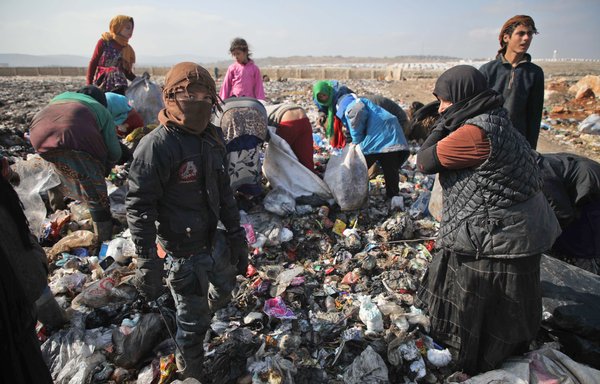 Displaced Syrian women and children sift through the trash for cans and food scraps at a landfill outside a camp in Kafr Lusin near the border with Turkey in Idlib province in 2019. Conditions like these enable groups like Russia's Wagner Group and ISIS to lure new recruits. [Aaref Watad/AFP]