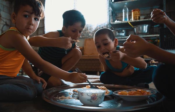 أطفال لاجئون سوريون يتشاركون وجبة غذاء داخل خيمتهم في منطقة البقاع. [حقوق الصورة لبرنامج الغذاء العالمي]