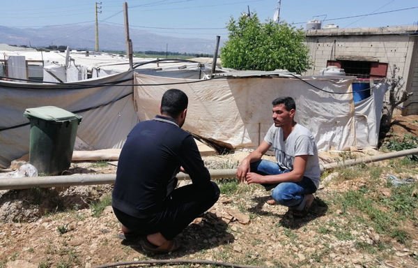 رجال سوريون يتحدثون أمام خيمتهم في مخيم مجدل عنجر في لبنان. [مزياد العلي/المشارق]