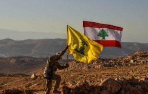 A Hizbullah fighter raises the militia's flag next to the national flag in Jurud Arsal near the Syrian border, underscoring the militia's control of the border with Syria. [Photo circulated on social media]
