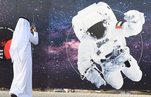 In this file photo taken September 25th, 2019 a man takes a picture of an illustration depicting an astronaut with the Emirati national flag outside Mohammed Bin Rashid Space Centre in Dubai. The first Arab space mission to Mars, set for launch next month to study the Red Planet's atmosphere, is designed to inspire the region's youth and pave the way for scientific breakthroughs. [Karim Sahib/AFP]