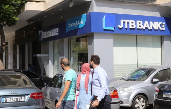 People walk past a branch of Jammal Trust Bank in Beirut's Hamra street on August 30th, 2019, a day after the US announced sanctions in Lebanon aimed at shutting down financing to Iran-backed Hizbullah. Powerful US financial sanctions were imposed on Jammal Trust Bank, which was accused of acting as a key financial institution for Hizbullah. [Anwar Amro/AFP]
