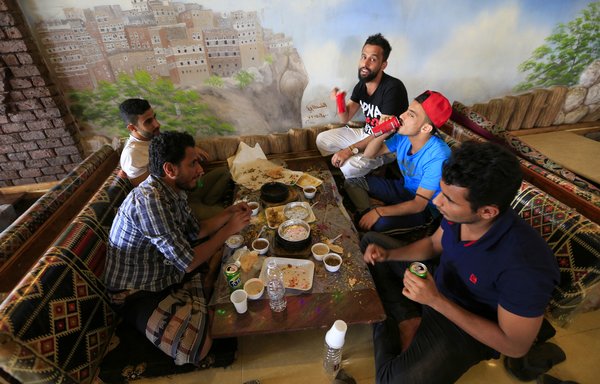 Yemeni men share a meal at a restaurant in Sanaa on July 16th, following the easing of measures against coronavirus. [Mohammed Huwais/AFP]