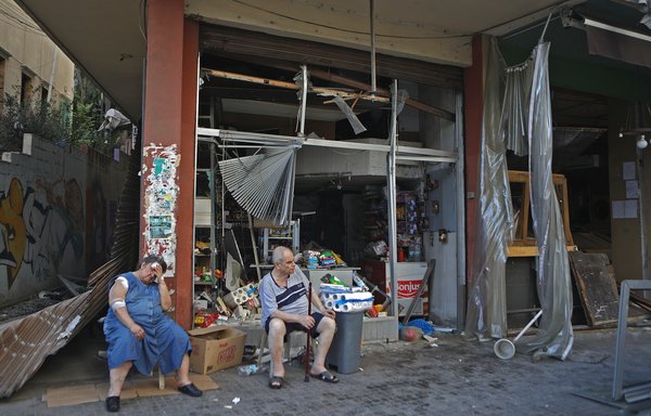 An injured Lebanese woman sits in front of her damaged shop in the trendy Beirut neighbourhood of Mar Mikhael on August 5th in the aftermath of a massive explosion in the Lebanese capital. [Patrick Baz/AFP]