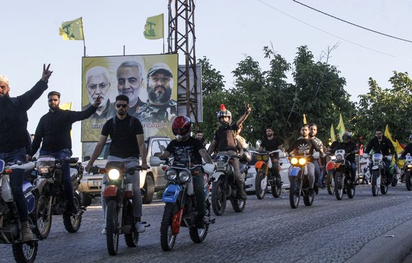 Hizbullah supporters ride motorcycles carrying the group's flags past a billboard showing the faces of slain Iraqi Popular Mobilisation Forces commander Abu Mahdi al-Muhandis, IRGC Quds Force commander Qassem Soleimani, and Hizbullah commander Imad Mughniyeh, in the southern Lebanese village of Adaisseh on May 25th. [Mahmoud Zayyat/AFP]