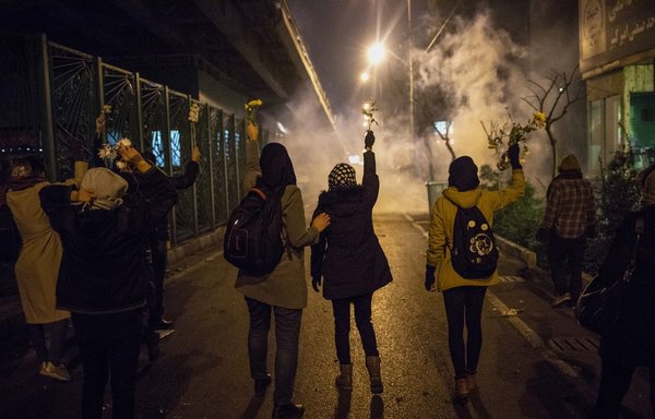Iranian protestors hold flowers as riot police fire tear gas during a demonstration in front of Tehran's Amir Kabir University on January 11th, after Iran admitted to having shot down a Ukrainian passenger jet by mistake on January 8th, killing all 176 people on board. [STR/AFP]
