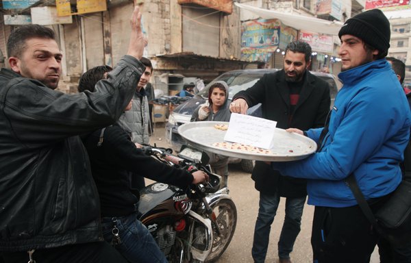 A Syrian man in the opposition-held town of Dana in northwestern Idlib Province offers sweets to children to mark the killing on January 3 of IRGC Quds Force commander Qasem Soleimani. [Aaref Watad/AFP]