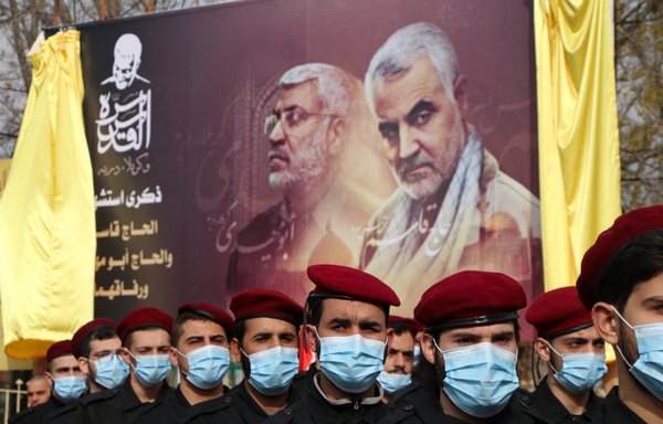 Members of Hizbullah take part in a parade under a large poster of slain Iraqi commander Abu Mahdi al-Muhandis and Iranian Revolutionary Guards commander Qassem Soleimani on January 2. [AFP]