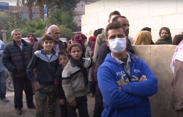 Syrians wait in line in the Damascus province city of Jaramana to receive their daily ration of bread. [Screenshot from video posted online by Q Street Journal]