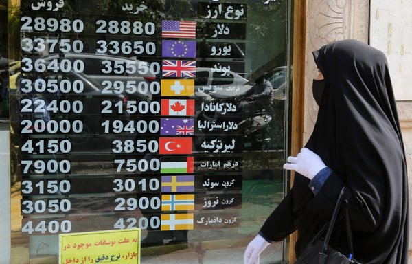 An Iranian woman checks a display board at a currency exchange shop as she walks past in Tehran, on September 29. [Atta Kenare/AFP]