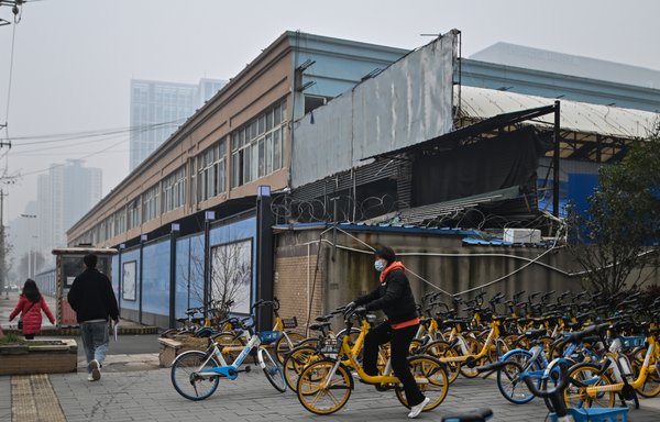 Pedestrians walk past the closed Huanan Seafood wholesale market in Wuhan, China, on January 23, one year after the city went into lockdown to curb the spread of COVID-19. [Hector Retamal/AFP]