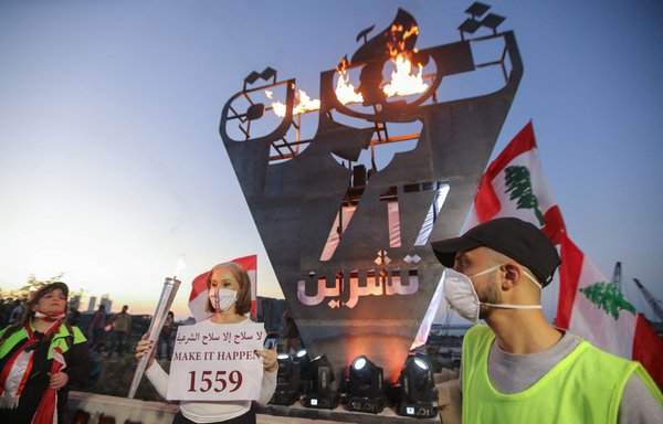 Lebanese protesters gather around the 'October 17 torch', lit to mark the one year anniversary of the beginning of a nationwide anti-government protest movement, in front of the devastated Beirut port, on October 17. Protesters' demands include, among other things, the disarmament of Hizbullah. [Anwar Amro/AFP]