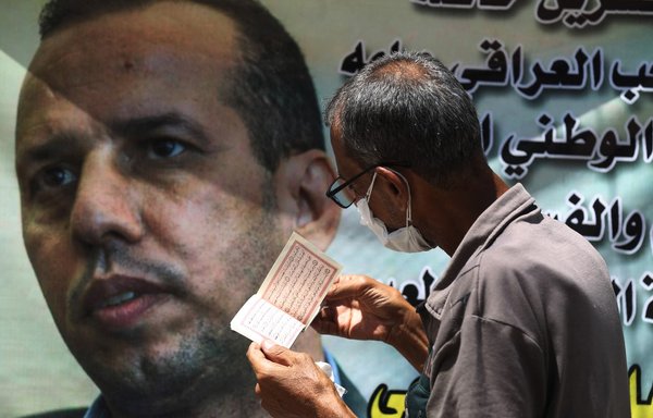 An Iraqi man recites verses from the Qur'an next to a poster of Iraqi extremism expert Hisham al-Hashemi, who was shot dead outside his house in Baghdad on July 6. [Ahmad al-Rubaye/AFP]
