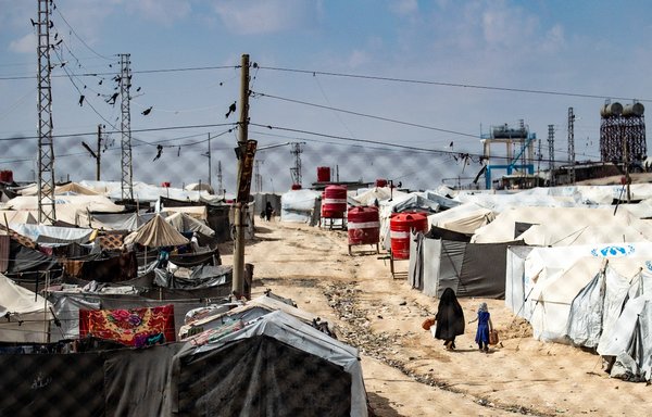 A woman and a child walk between tents at al-Hol camp, which holds relatives of ISIS fighters, in northeastern Syria's al-Hasakeh province on March 3. [Delil Souleiman/AFP]