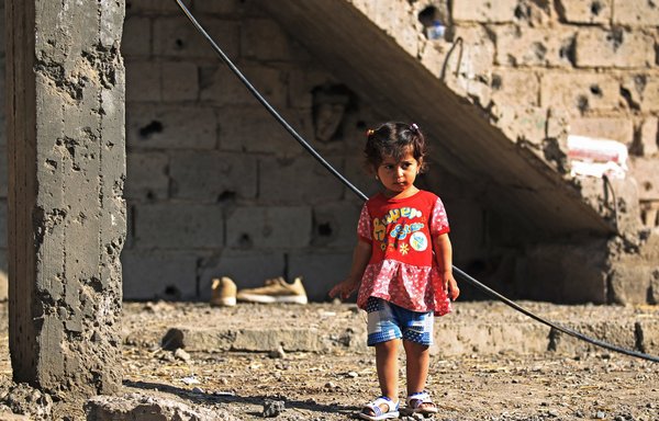 An Iraqi girl stands outside of a house damaged by a rocket fired by Iran-backed militia members near Baghdad airport last September. [Ahmad al-Rubaye/AFP]