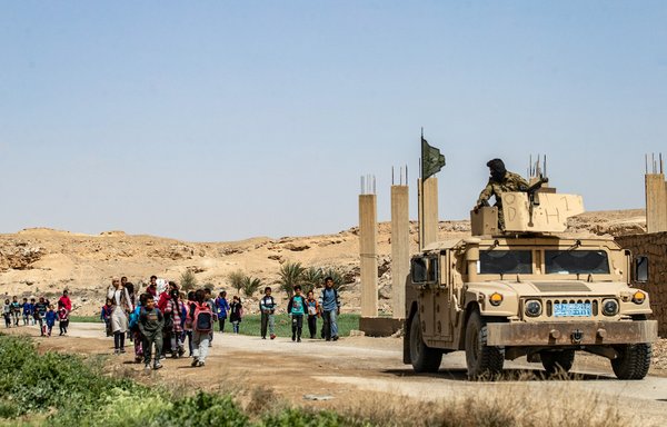 Fighters of the Kurdish-led Syrian Democratic Forces (SDF) stand guard as students return home from school in the village of al-Baghouz in Syria's northern Deir Ezzor province, on March 24. [Delil Souleiman/AFP]