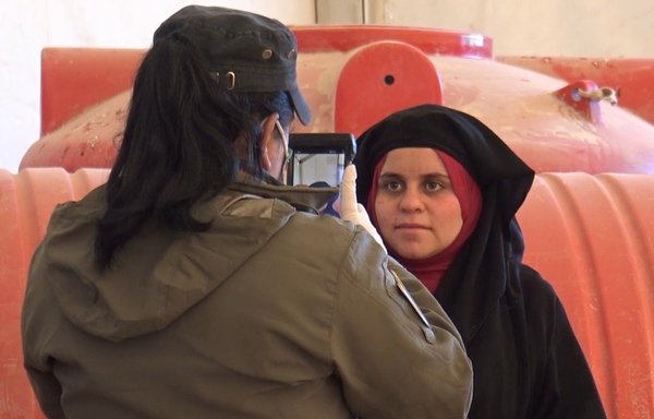 A female member of the security forces photographs and takes a retina scan of a resident at al-Hol camp to update a biometrics database. [SDF Co-ordination and Military Operations Centre]