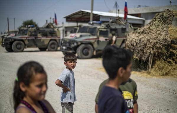 Syrian children watch as Russian soldiers reposition in Derouna Arha near the Syrian border with Turkey on June 16. [Delil Souleiman/AFP]