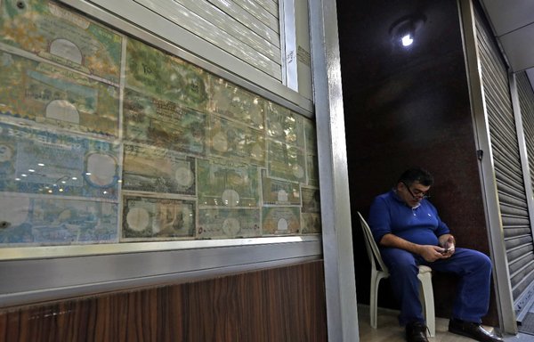 A man sits in front of a closed money exchange office in Beirut on November 29, 2019. [Joseph Eid/AFP]