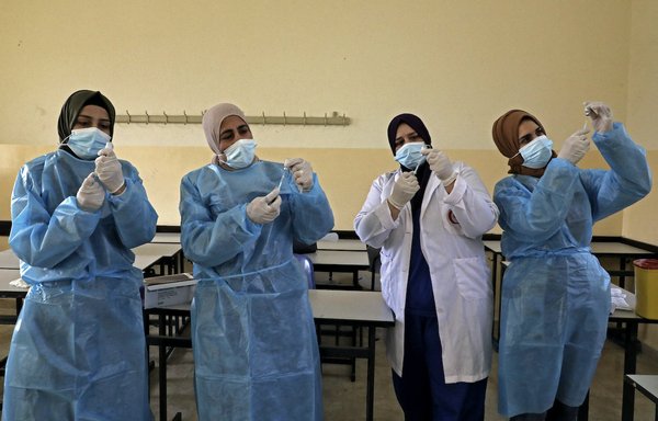 Palestinian Health Ministry workers prepare doses of the Sinopharm COVID-19 coronavirus vaccine, donated by the Chinese government, at a school in Halhoul, north of Hebron on the occupied West Bank, on April 6. [Hazem Bader/AFP]