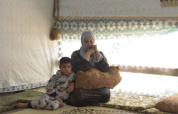 اللاجئة السورية رحمة العلي تجلس مع ابنها محمد داخل خيمتهم في مخيم مجدل عنجر بلبنان. وكان محمد وأخته ريان يشاركان في مدرسة افتراضية من خيمتهما. [زياد حاتم/المشارق]