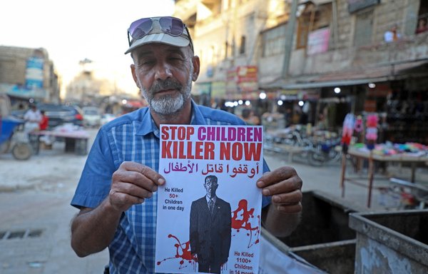 A Syrian man holds a poster depicting Syrian President Bashar al-Assad as a killer in the Idlib province town of Dana on May 24. [Aaref Watad/AFP]