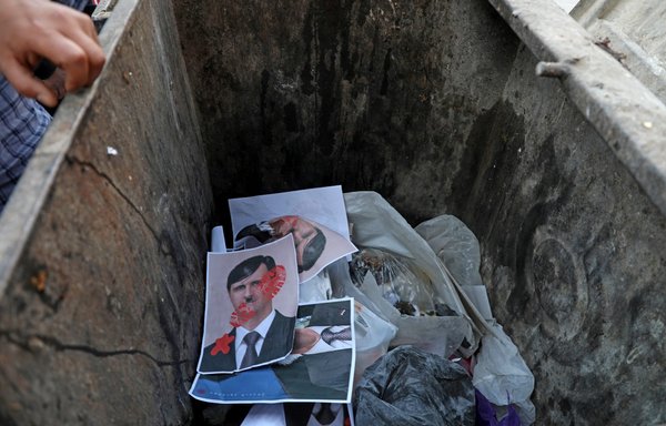 Syrians throw posters depicting Syrian President Bashar al-Assad as Adolf Hitler in a garbage bin symbolising a ballot box in the Idlib province town of Dana on May 24. [Aaref Watad/AFP]
