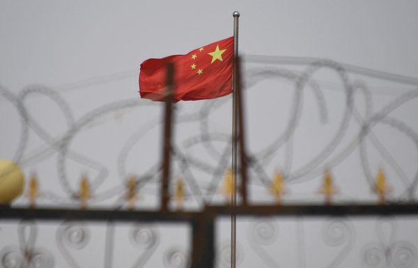This photo taken on June 4, 2019, shows the Chinese flag behind razor wire at a housing compound in Yangisar, Xinjiang region, China. [Greg Baker/AFP]