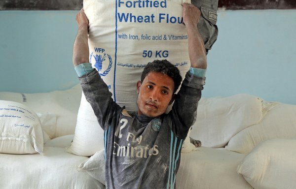 A young man lifts a sack of flour provided by the World Food Programme in the Yemeni city of Sanaa on June 1. [Mohammed Huwais/AFP]