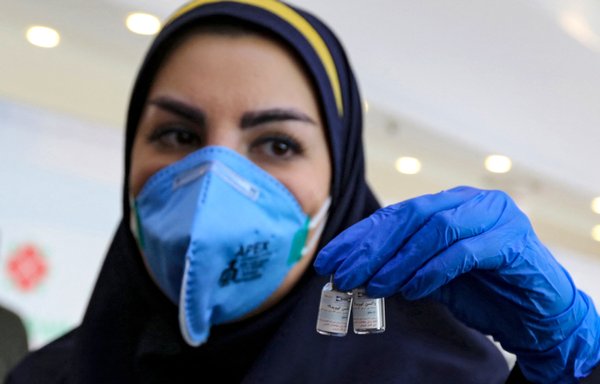 A health worker displays a vial of the Iranian COVID-19 vaccine during the second phase of trials in Tehran on March 15. [Atta Kenare/AFP]