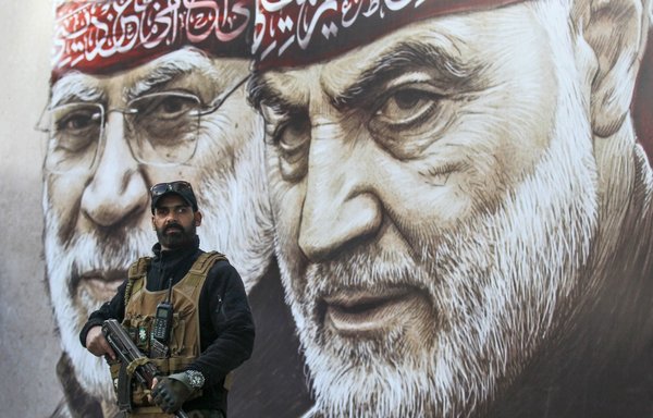 A militiaman stands guard beneath posters displaying portraits of slain IRGC Quds Force commander Qassem Soleimani and Abu Mahdi al-Muhandis on January 2. [Ahmad al-Rubaye/AFP]
