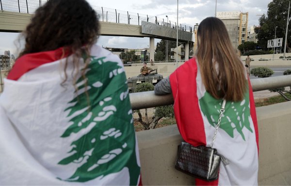 Lebanese protesters, draped in national flags, take part in a rally pressing the president to call for parliamentary elections, on a road leading to the presidential palace near Beirut on December 1, 2019. [Anwar Amro/AFP]