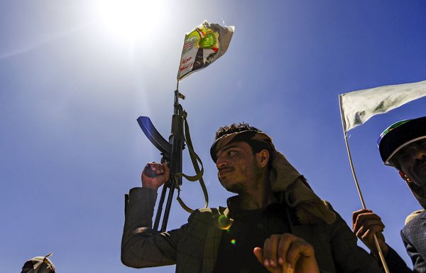 A Yemeni man holds up a Kalashnikov assault rifle with a flag sticking from its barrel showing a picture of Houthi leader Abdulmalik al-Houthi, during a tribal meeting in Sanaa on September 21, 2019. [Mohammed Huwais/AFP]