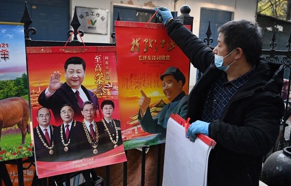 یک فروشنده روز ۱۳ آبان گذشته در بازاری در حال کنار گذاشتن تقویم های سال ۱۴۰۰ است. در این تقویم ها تصاویر مائو تسه تونگ، رهبر فقید کمونیستی (راست)، و شی جین پینگ، رئیس جمهوری کنونی چین (بالا، چپ)، بالای عکس چهار دانشمند پزشکی قرار دارد که به دلیل تلاش هایشان در مبارزه با ویروس کرونا و بیماری کووید-۱۹ جوایزی را دریافت کرده بودند. [گرگ بیکر/ خبرگزاری فرانسه]