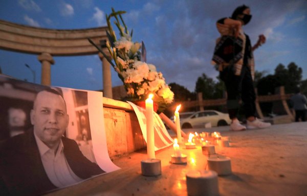 An Iraqi places a candle in front of a poster of slain Iraqi extremism expert Hisham al-Hashemi, who was shot dead outside his house in Baghdad, during a candlelight vigil in Erbil on July 11, 2020. [Safin Hamed/AFP]