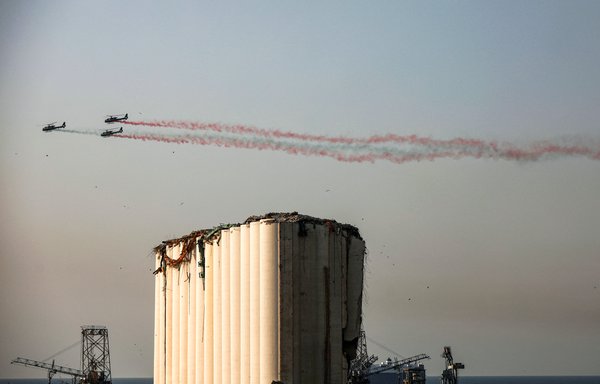 Lebanese army helicopters release smoke in the colours of the national flag during a flyover by the damaged grain silos at the port of Beirut on August 4, during a remembrance ceremony on the first anniversary of the blast that ravaged the port and the city. [Patrick Baz/AFP]