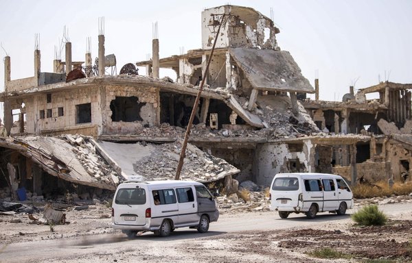 Local transport microbuses are seen driving past destroyed buildings in an opposition-held neighbourhood of the southern Syrian city of Daraa in this file photo from October 2, 2018. [Mohamad Abazeed/AFP]