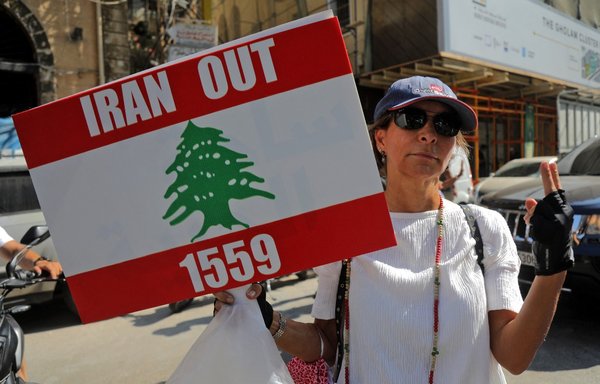 A demonstrator holds up a sign asking for Iran to seize its interference in Lebanon according to UN Security Council Resolution 1559, in the Gemmayze neighbourhood as protesters head towards the port of Beirut on August 4, on the first anniversary of the blast that ravaged the port and the city. [Ibrahim Amro/AFP]